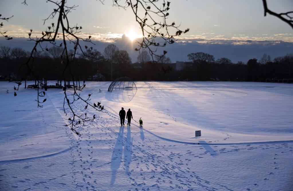 A couple walks their dog through a snow covered Piedmont Park as the sun rises in Atlanta, Wednesday, Jan. 17, 2018. The South awoke on Wednesday to a two-part Arctic mess. First came a thin blanket of snow and ice, and then came the below-zero wind chills and record-breaking low temperatures in New Orleans and other cities. (AP Photo/David Goldman)