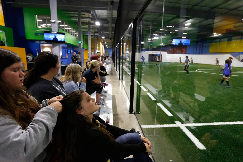 Holly Espinoza, 14, left, braids her twin sister Amanda's hair as they watch women's soccer league action on one of the Sports City indoor fields at the Epicenter sports complex in Santa Rosa, California on Thursday, October 13, 2016. (Alvin Jornada / The Press Democrat)