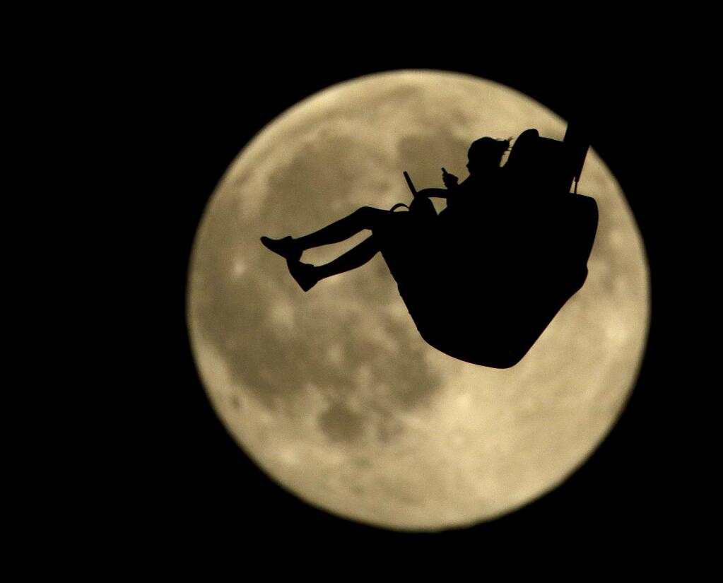 A girl is silhouetted against a rising full moon as she ride an attraction at Worlds of Fun amusement park Thursday, July 30, 2015, in Kansas City, Mo. When the full moon appears at 6:43 a.m. EDT (1043 GMT) in the U.S. Friday, it will become the second full moon of July. Geoff Chester of the U.S. Naval Observatory said the traditional definition of a blue moon is two full moons in a month. (AP Photo/Charlie Riedel)