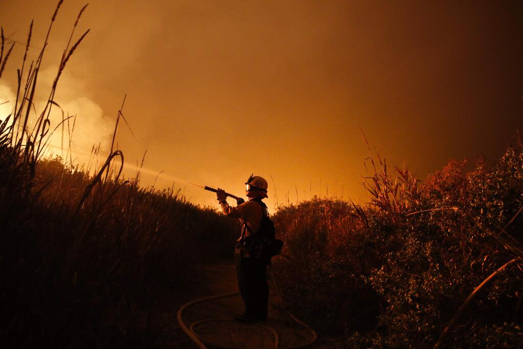 FILE - In this Dec. 7, 2017, file photo, firefighter Ryan Spencer battles a wildfire as it burns along a hillside toward homes in La Conchita, Calif. With three strong hurricanes, wildfires, hail, flooding, tornadoes and drought, supersized weather disasters tallied a record high bill for America last year: $306 billion. (AP Photo/Jae C. Hong, File)
