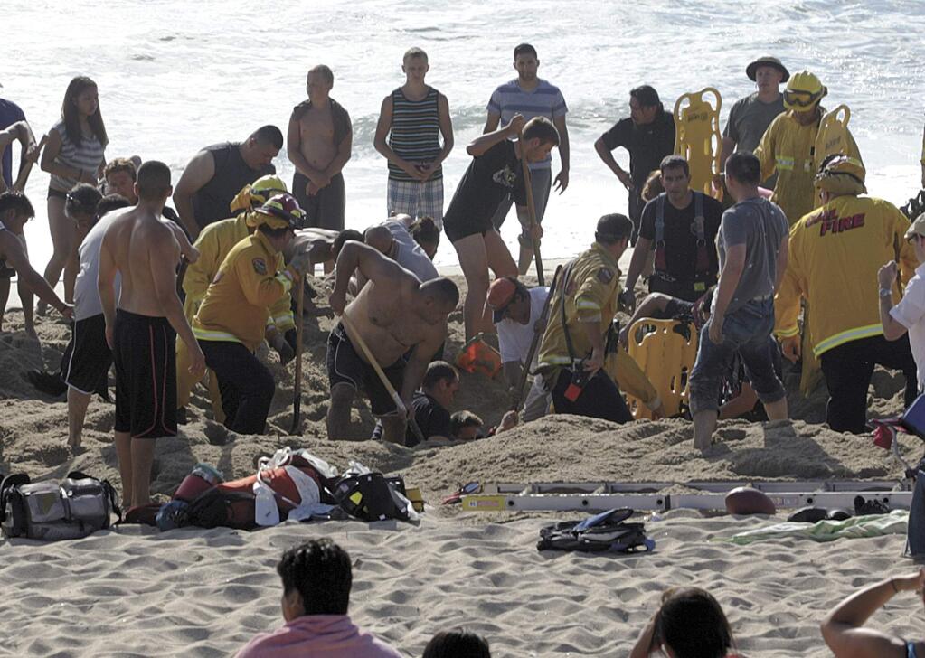 This Monday, July 21, 2014, photo released by the Half Moon Bay Review shows emergency crew workers and volunteers working to rescue a man at Francis State Beach in Half Moon Bay. Authorities say a young man has died after a hole he dug on a Northern California beach collapsed and trapped him in the sand for at least five minutes. (AP Photo/Half Moon Bay Review, Dean Coppola)