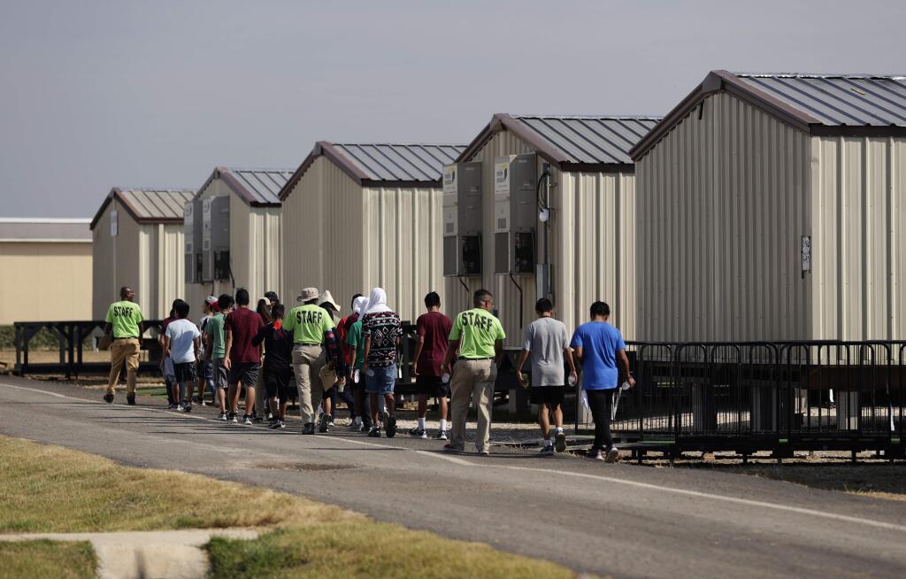 FILE - In this July 9, 2019, file photo, staff escort immigrants to class at the U.S. government's newest holding center for migrant children in Carrizo Springs, Texas. The Trump administration will make a case in court to end a longstanding settlement governing detention conditions for immigrant children, including how long they can be held by the government. A hearing is scheduled before a federal judge Friday, Sept. 27, in Los Angeles over the so-called Flores settlement. (AP Photo/Eric Gay, File)
