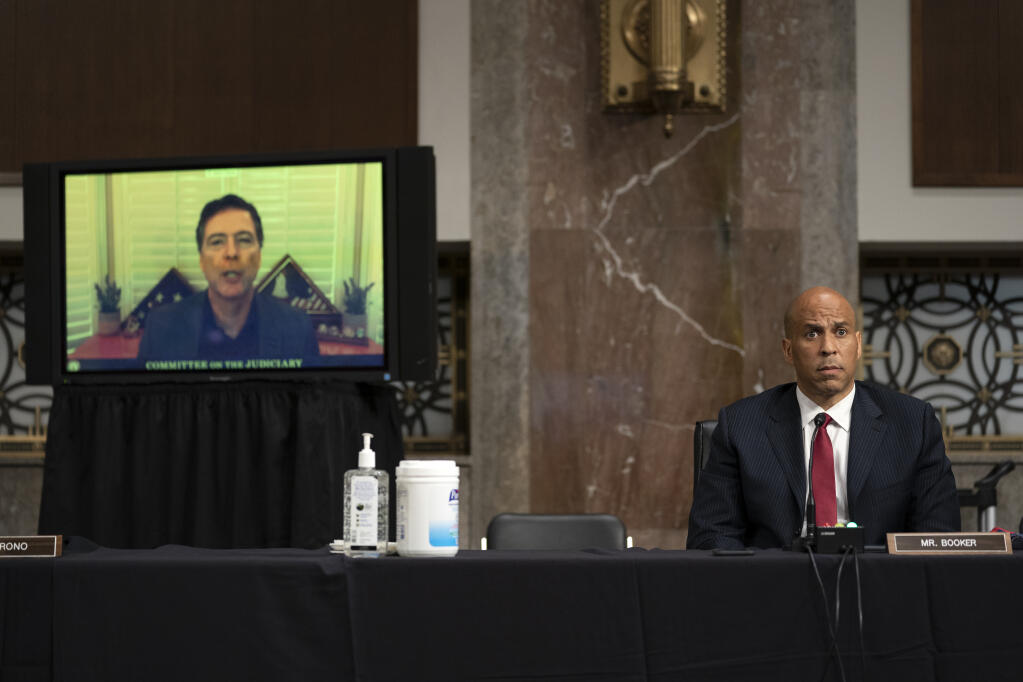 Sen. Cory Booker, D-N.J., listens as James Comey, former director of the Federal Bureau of Investigation, speaks virtually, left, during a Senate Judiciary Committee hearing on Capitol Hill in Washington, Wednesday, Sept. 30, 2020, to examine the FBI "Crossfire Hurricane" investigation. (Stefani Reynolds/Pool via AP)
