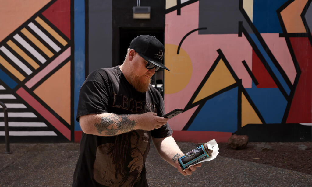 Justin Hollingsworth makes a video of his Free Art Friday work, which he will post to Instagram, used as clues to where he will hide the item, in this case, on the backside of the Third Street parking garage, Friday, April 29, 2022 in Santa Rosa. (Kent Porter / The Press Democrat) 2022