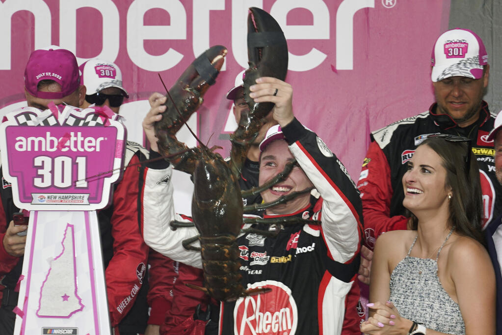 Christopher Bell holds up a giant lobster while celebrating with his wife, Morgan, right, after winning a NASCAR Cup Series auto race at the New Hampshire Motor Speedway, Sunday, July 17, 2022, in Loudon, N.H. (AP Photo/Charles Krupa)