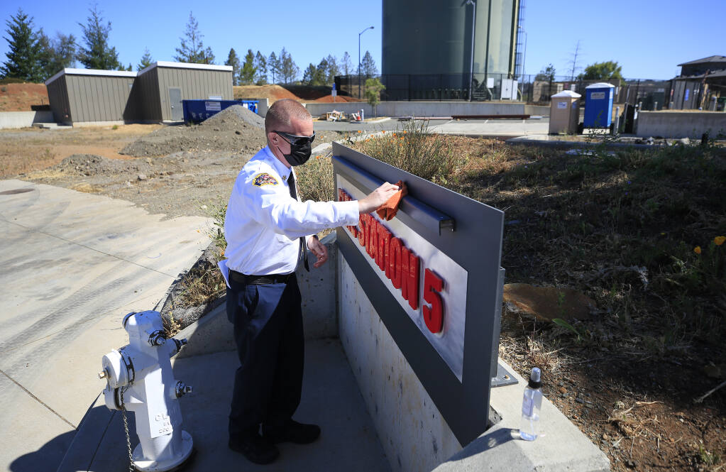 Santa Rosa Fire Chief Scott Westrope cleans graffiti from a sign at the former Station 5 in Fountaingrove Tuesday, May 25, 2021, one of the few firehouse landmarks remaining since the 2017 Tubbs fire burned the station to the ground. (Kent Porter / The Press Democrat) 2021