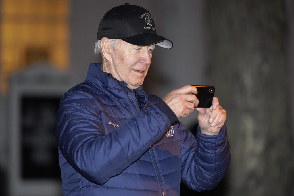 President Joe Biden uses his phone while waiting for the annual Christmas Tree Lighting ceremony to begin in Nantucket, Mass., Friday, Nov. 25, 2022. (AP Photo/Susan Walsh)