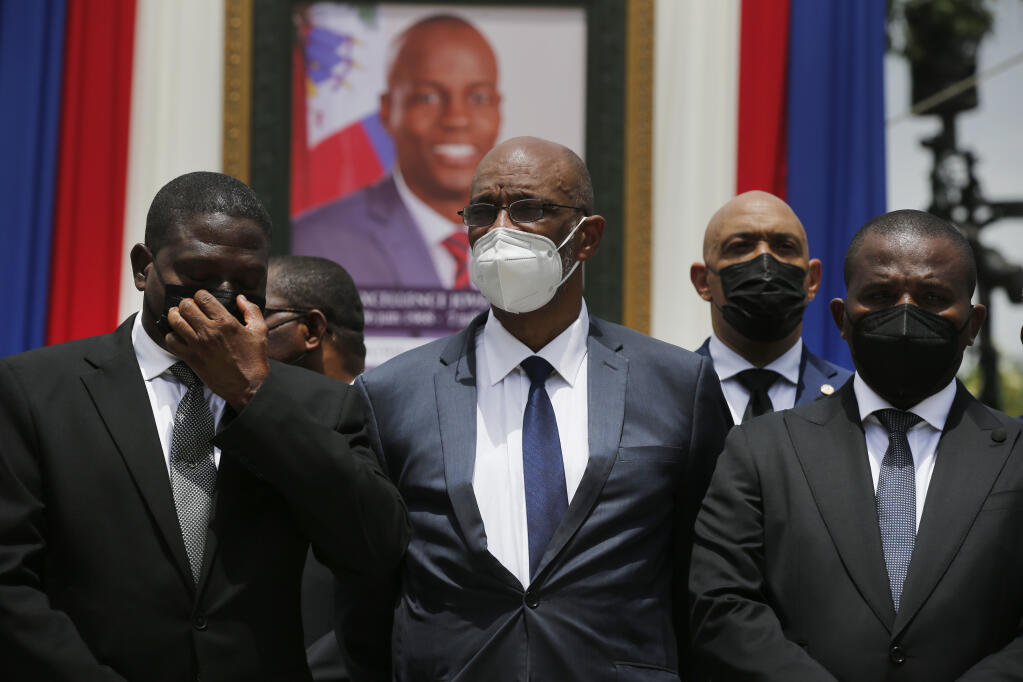 FILE - In this July 20, 2021 file photo, Haiti's designated Prime Minister Ariel Henry, center, and interim Prime Minister Claude Joseph, right, pose for a group photo with other authorities in front of a portrait of slain Haitian President Jovenel Moise at the National Pantheon Museum during a memorial service for Moise in Port-au-Prince, Haiti. Haiti’s chief prosecutor has asked a judge to charge Henry in the slaying of his predecessor and barred him from leaving the country. (AP Photo/Joseph Odelyn, File)