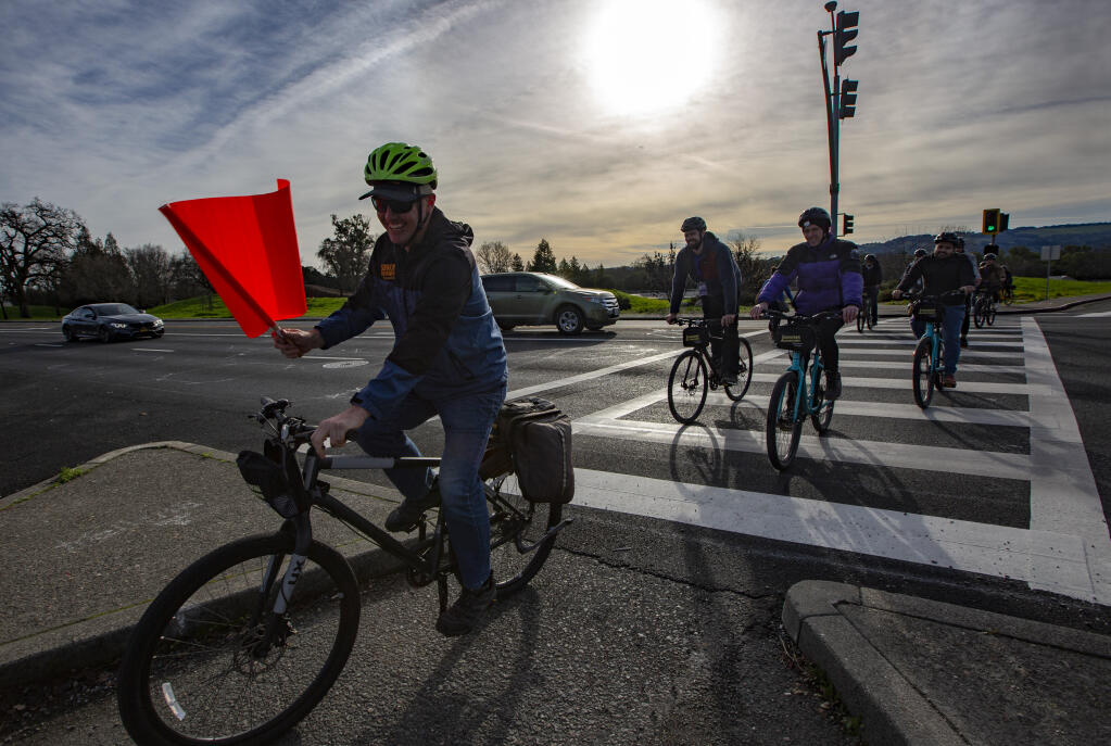 Using one of the safety flags, a group of bicyclists crosses Highway 12 to Verano Avenue on Thursday, Jan. 19, 2023. Buckets filled with fluorescent flags, along with instructions on how to use them, were placed at every Verano Avenue and Highway 12  pedestrian crossing. (Robbi Pengelly/Index-Tribune)