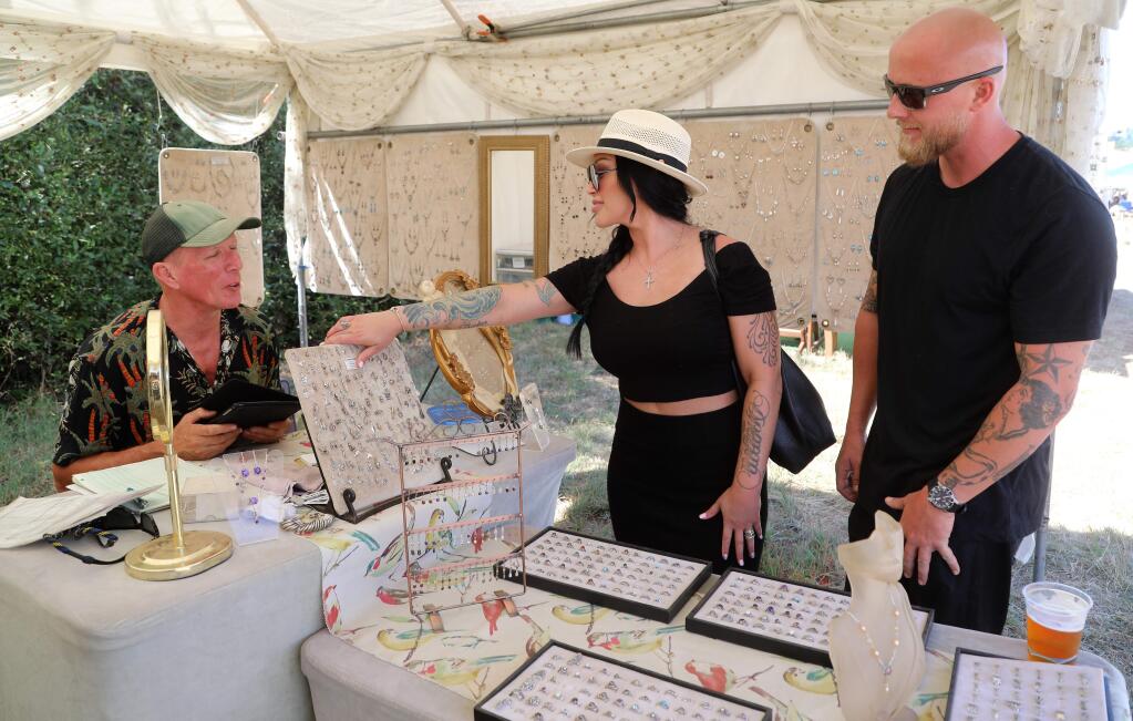 Andrea Battensby tries on jewelry by designer Jason Dayne (left) as Matt Buhrer looks on at the Bodega Seafood, Art and Wine Festival in Bodega on Sunday, Aug. 25, 2019. (WILL BUCQUOY/FOR THE PD)