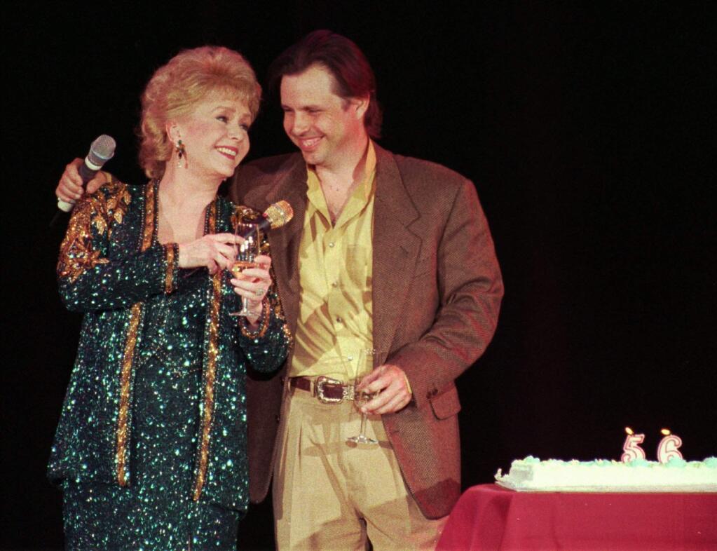 FILE - In this April 1, 1997, file photo, Debbie Reynolds, left, celebrates her 65th birthday on stage as her son, Todd Fisher, presents her with a cake following her evening variety show, at the Debbie Reynolds Hotel in Las Vegas. Fisher told Entertainment Tonight for an interview published online on March 22, 2017, that Reynolds set him up “for her leaving the planet” the day his sister and Reynolds' daughter Carrie Fisher died in December 2016. (AP Photo/Lennox McLendon, File)