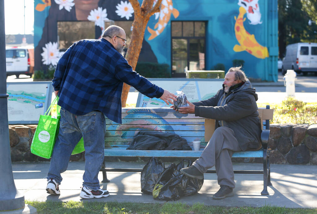 Ray Tilton hands a package of socks and gloves to a homeless person at Prince Gateway Park in Santa Rosa, Tuesday, Jan. 24, 2023.  (Christopher Chung/The Press Democrat)