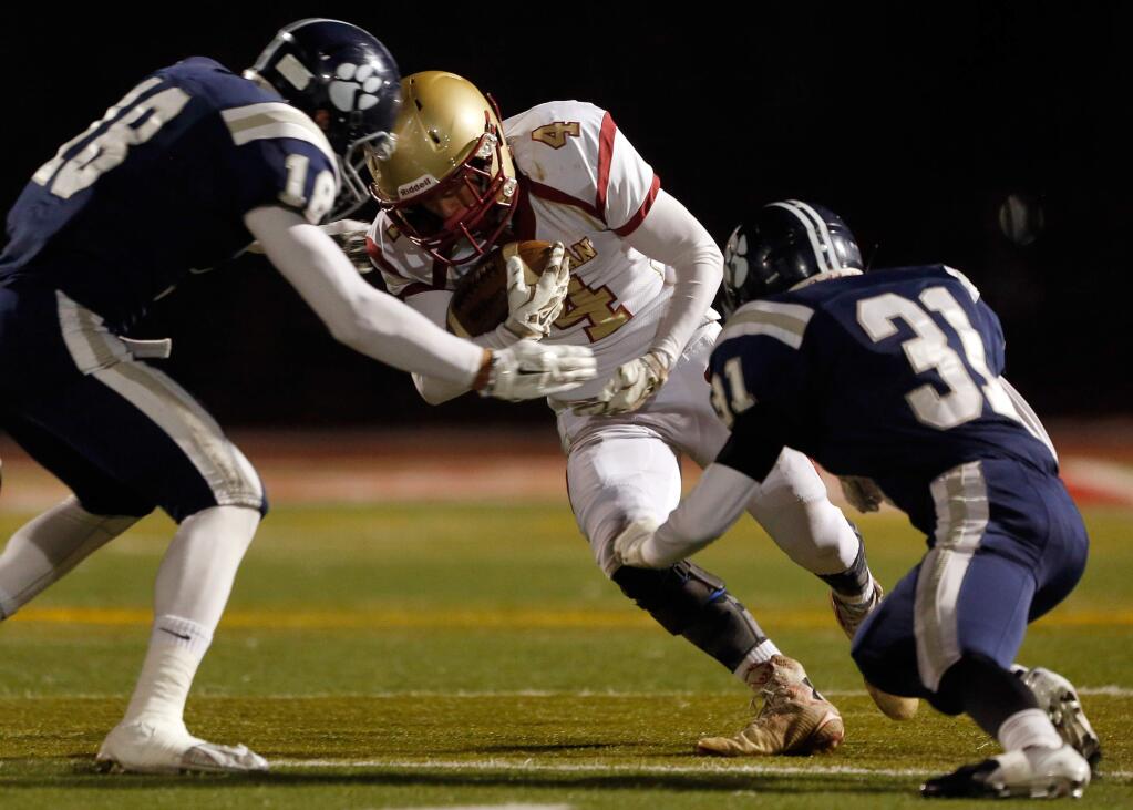 Cardinal Newman's Sammy Bossard (4) takes a hit from Marin Catholic's Zack Margulis (18) and Nader Afrakhan (31) during the first half of the NCS Division 4 championship football game between Cardinal Newman and Marin Catholic high schools in Rohnert Park, California on Saturday, December 5, 2015. (Alvin Jornada / The Press Democrat)