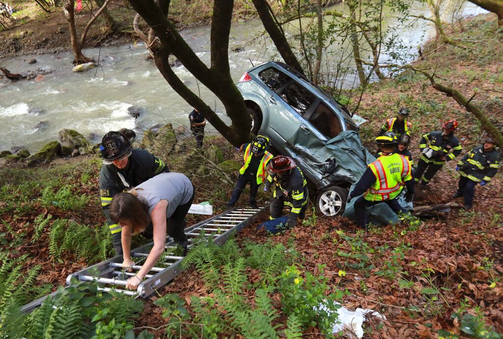 Santa Rosa firefighters remove a woman driver through the front window after an accident that pinned the vehicle between two trees near above Santa Rosa creek on Montgomery Dr. on Tuesday afternoon, February 14, 2017. (John Burgess/The Press Democrat)