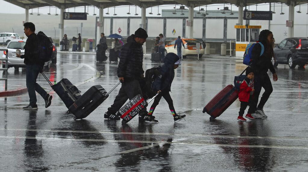 Travelers walk during a rainstorm to the terminals at Oakland International Airport, Friday, April 6, 2018, in Oakland, Calif. (AP Photo/Ben Margot)