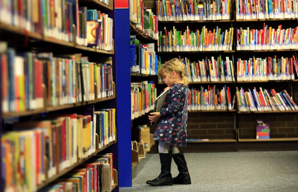 Aria Beirne, 3, of Santa Rosa looks through the stack of books in the children's section at the Sonoma County Central Library in Santa Rosa on Tuesday, January 3, 2017. (John Burgess/The Press Democrat)