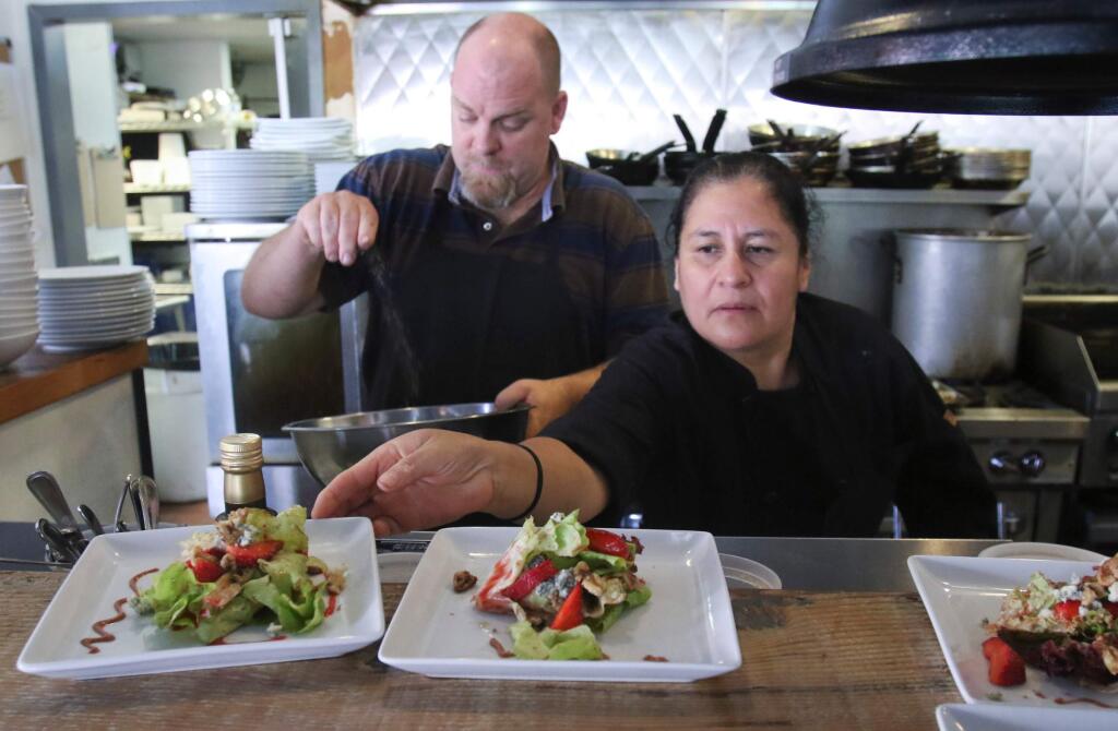 Garrett Adair, chef and owner of Bistro 100, cooks in the background while Chef Rosaura puts the finishing touches on salads during the 'Taste of Petaluma' preview lunch at Bistro 101 in Petaluma on Wednesday, August 13, 2015. (SCOTT MANCHESTER/ARGUS-COURIER STAFF)