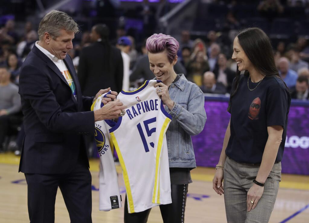 Golden State Warriors CEO Rick Welts, left, presents jerseys to soccer player Megan Rapinoe (15) and basketball player Sue Bird, right, during the first half of the Warriors' NBA basketball game against the Phoenix Suns on Wednesday, Oct. 30, 2019, in San Francisco. (AP Photo/Ben Margot)