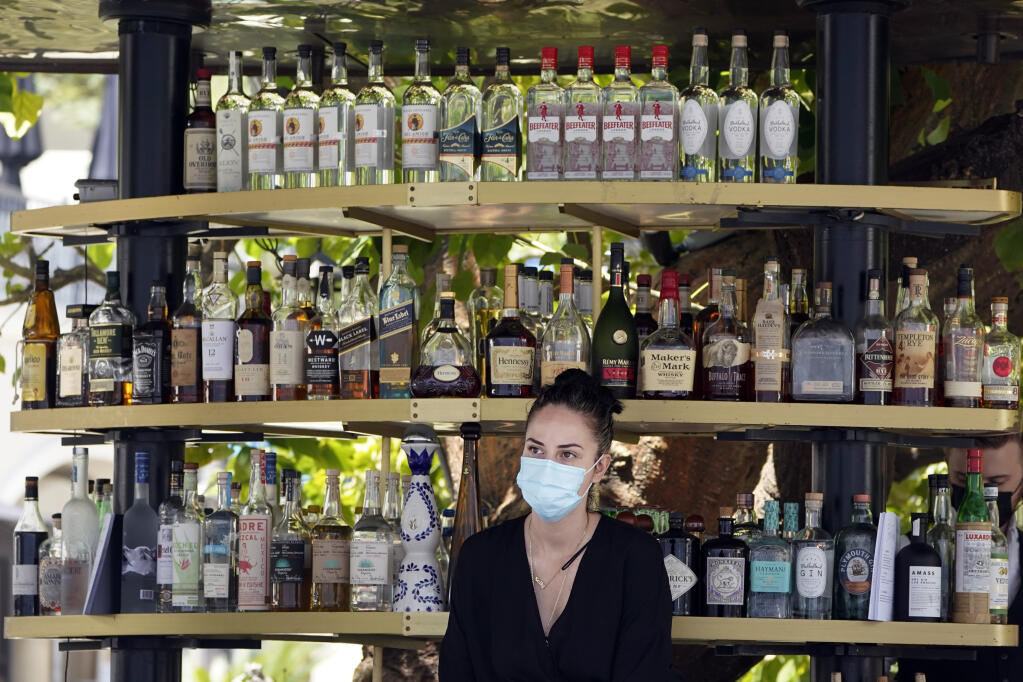 FILE - In this May 20, 2021, file photo, a bartender wears a mask while working at an outdoor bar amid the COVID-19 pandemic, at The Grove in Los Angeles. California workplace regulators are considering Thursday, June 3, 2021, whether to end mask rules if every employee in a room has been fully vaccinated against the coronavirus, frustrating business groups by eying a higher standard than the state plans to soon adopt for social settings. (AP Photo/Marcio Jose Sanchez, File)