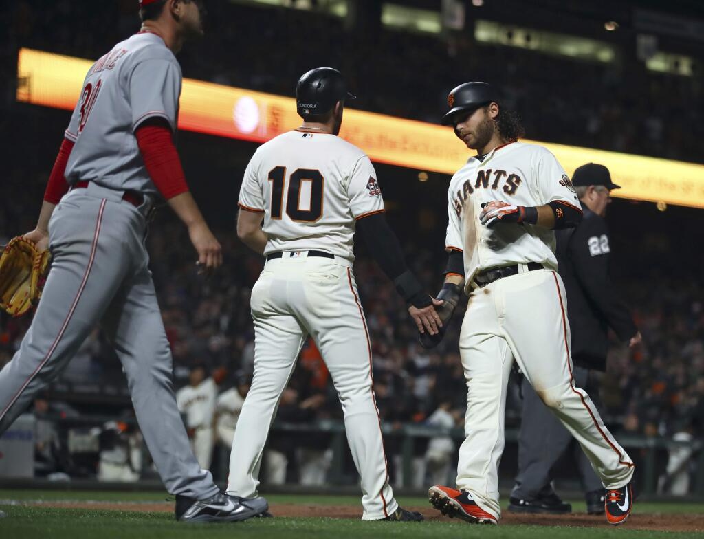 The San Francisco Giants' Evan Longoria (10) and Brandon Crawford celebrate after scoring as Cincinnati Reds' Tyler Mahle, left, walks back to the mound during the fourth inning Tuesday, May 15, 2018, in San Francisco. Both scored on a single by Pablo Sandoval. (AP Photo/Ben Margot)