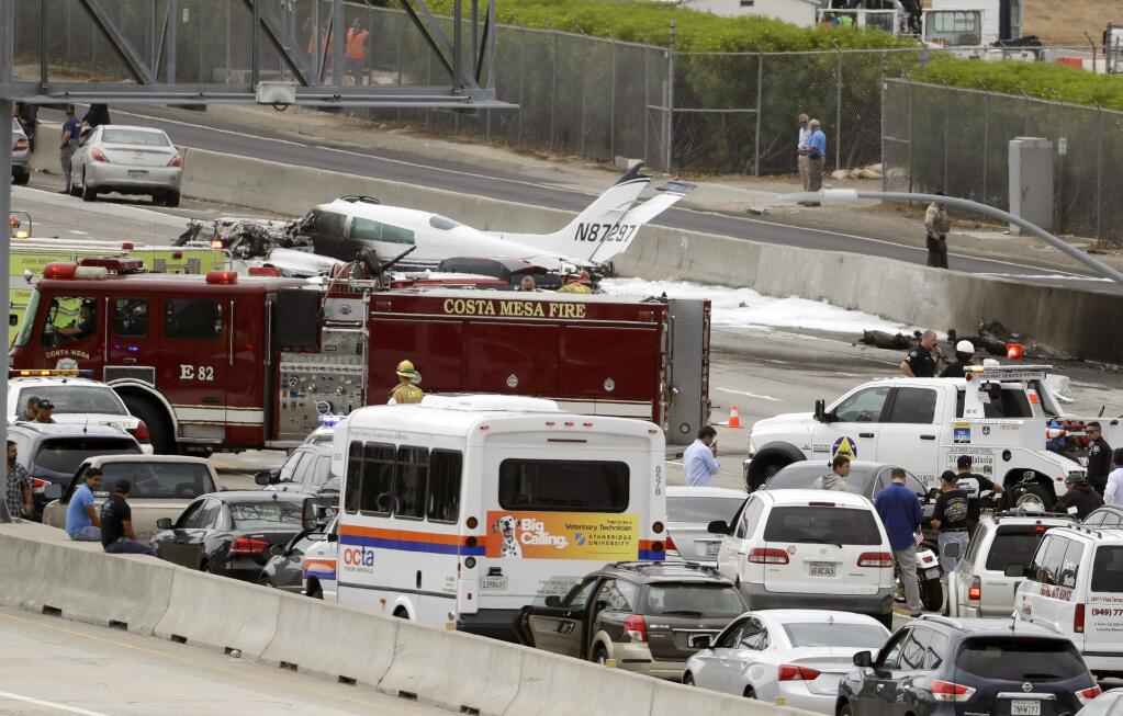 Emergency responders gather round the crash of a Cessna 310 aircraft on Interstate 405, just short of a runway at John Wayne Airport in Costa Mesa, Calif., Friday, June 30, 2017. Two people were injured in the small plane crash. (AP Photo/Chris Carlson)