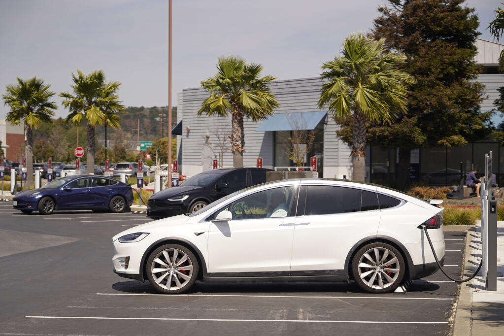A man talks on his phone while sitting in his electric car at a Tesla charging station on April 2, 2021, in Marin City. (AP Photo/Eric Risberg)