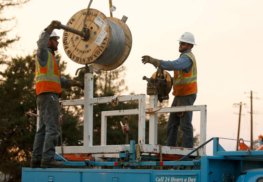 PG&E workers Gary Callinan, left, and Jesse Guin load a 2,500-foot spool to be used to provide backup tension for a power line their crews are stringing across Highway 101 to restore power to parts of north Santa Rosa, California on Wednesday, Oct. 11, 2017. (Alvin Jornada / The Press Democrat)