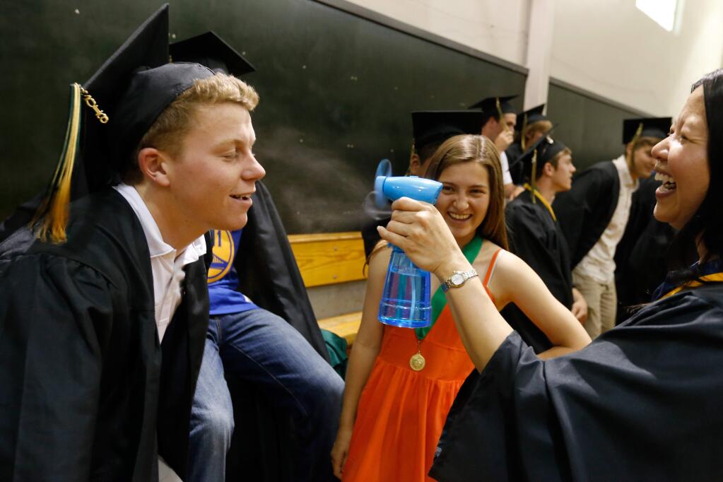Sean Nagle, left, cools off with a spritz from math teacher Cindy Lui's misting fan before the Maria Carrillo High School commencement exercises in Santa Rosa, California on Friday, June 3, 2016. (Alvin Jornada / The Press Democrat)