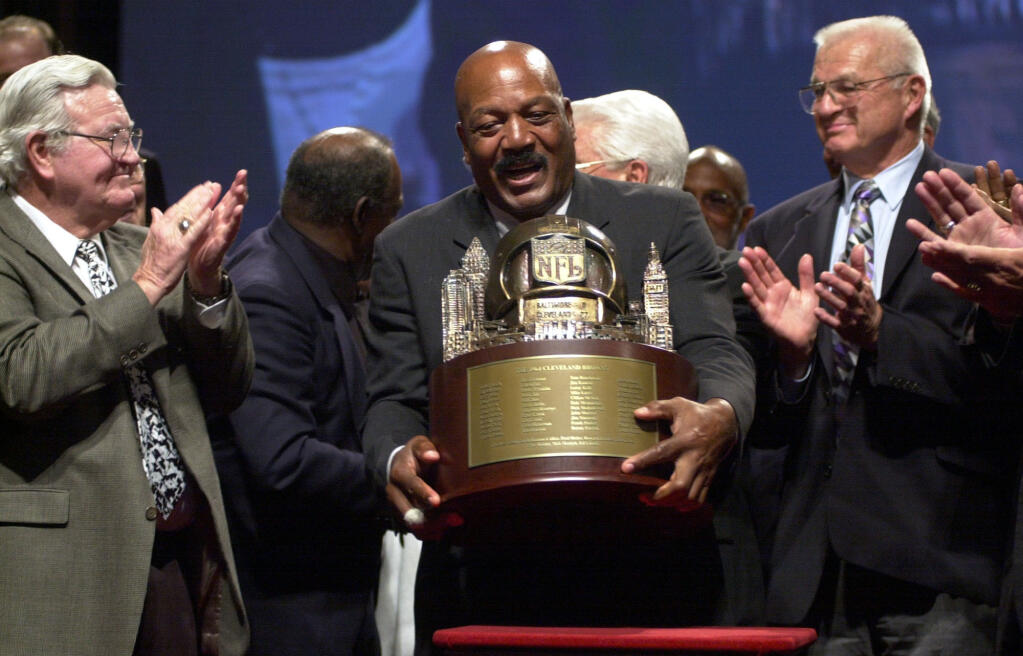 FILE - Jim Brown, center, picks up a trophy presented by NFL Commissioner Paul Tagliabue, to the members of Cleveland Browns 1964 Championship Team, at Severance Hall in Cleveland, Friday, Sept. 10, 2004. At left is Bernie Parish, and at right Paul Wiggin. The original trophy presented to the team after their 1964 victory over the Baltimore Colts is in the possession of the Green Bay Packers, who were the 1965 Championship Team. NFL legend, actor and social activist Jim Brown passed away peacefully in his Los Angeles home on Thursday night, May 18, 2023, with his wife, Monique, by his side, according to a spokeswoman for Brown's family. He was 87. (AP Photo/Jamie-Andrea Yanak, File)