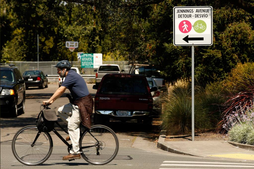 A bicyclist pedals along North Dutton Avenue past a detour sign directing pedestrian and bicycle traffic past Jennings Avenue, where a planned SMART rail crossing hasn't been built. (ALVIN JORNADA / The Press Democrat)