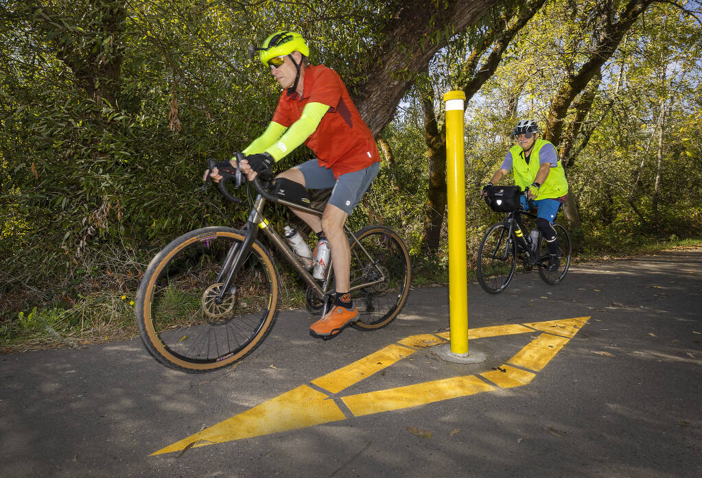Don Keylon, left, and Tom Taylor bike past a bollard on the West County Regional Trail at Green Valley Road in Graton October 11, 2022. Sonoma County Regional Parks repainted the bollards and added the yellow diamond on the ground for added visibility after the death of chef Rob Reyes in August. (John Burgess/The Press Democrat)