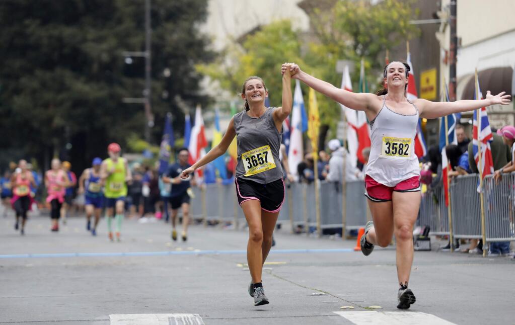 Amy Maslivec, left, and Ashley Armstrong hold hands as they near the finish line of the Santa Rosa Half Marathon down Fourth Street in Santa Rosa on Aug. 26, 2018. (Beth Schlanker/ The Press Democrat)