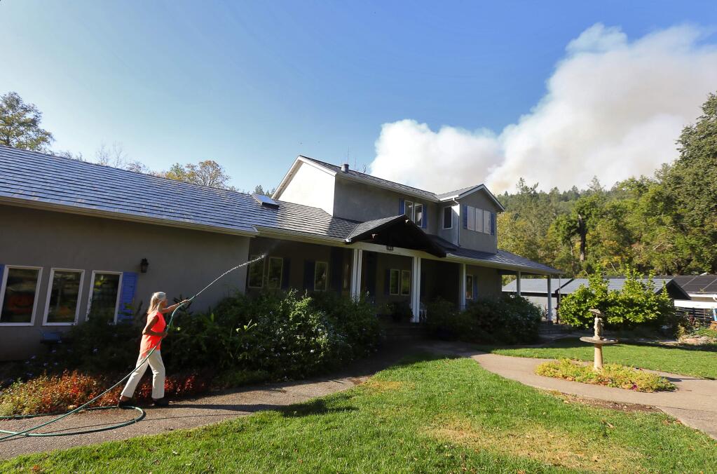 Diane Trembley, 83, hoses down her home along Adobe Canyon Road, as smoke from Hood Mountain Regional Park and Sugarloaf Ridge State Park on Sunday, October 15, 2017. (Christopher Chung/ The Press Democrat)