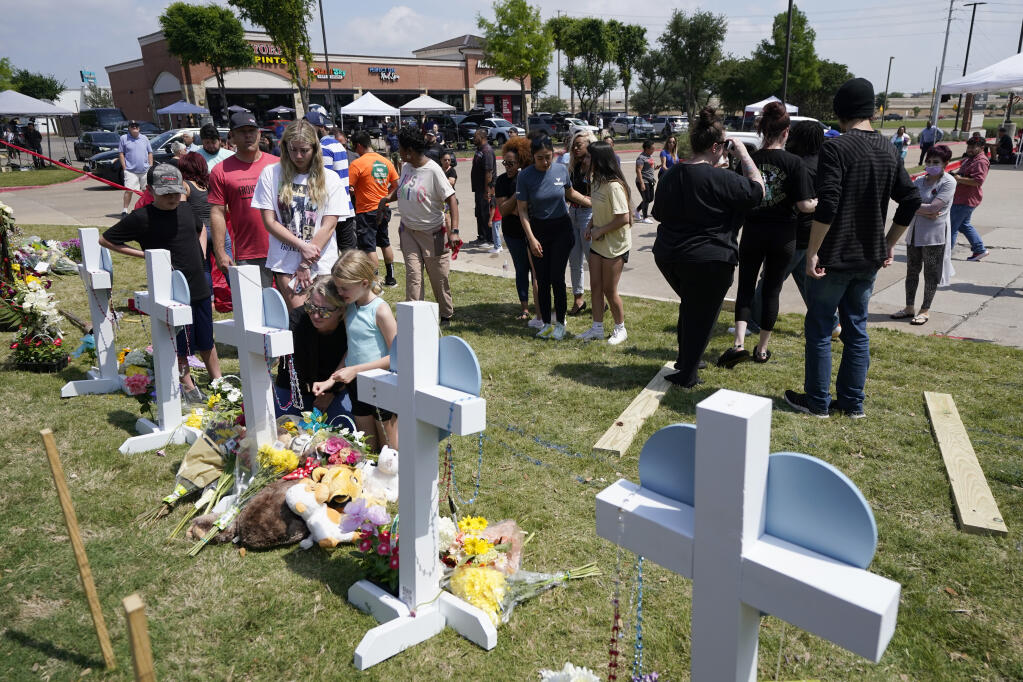 Jessica Himes, kneeling in front of cross, holds her daughter Harper, blue shirt, as her son Hudson, left in black shirt, her husband Scott, left rear in red shirt, and daughter Blakely Brooks, center left in white shirt, all from Allen, Texas, look on at a makeshift memorial by the mall where several people were killed in Saturday's mass shooting, Monday, May 8, 2023, in Allen, Texas. (AP Photo/Tony Gutierrez)