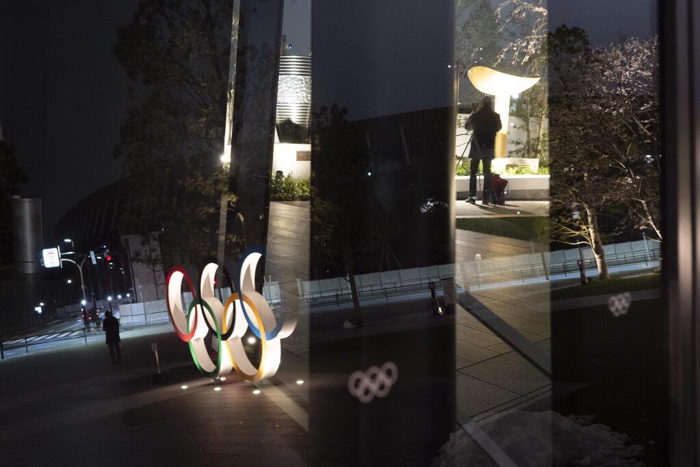 The Olympic rings are reflected on the facade of Japan Olympic Museum Monday, March 30, 2020, in Tokyo. The Tokyo Olympics will open next year in the same time slot scheduled for this year's games. Tokyo organizers said Monday the opening ceremony will take place on July 23, 2021. (AP Photo/Jae C. Hong)