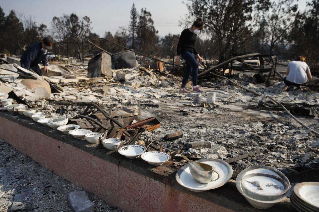 A set of salvaged china that Karen Curzon, background center, inherited from her grandmother lie on the foundation of her home that was destroyed by a wildfire in the Coffey Park neighborhood. On Oct. 15, 2017 she said, 'We are going to rebound, rebuild and get this community back.' (AP Photo/Jae C. Hong)