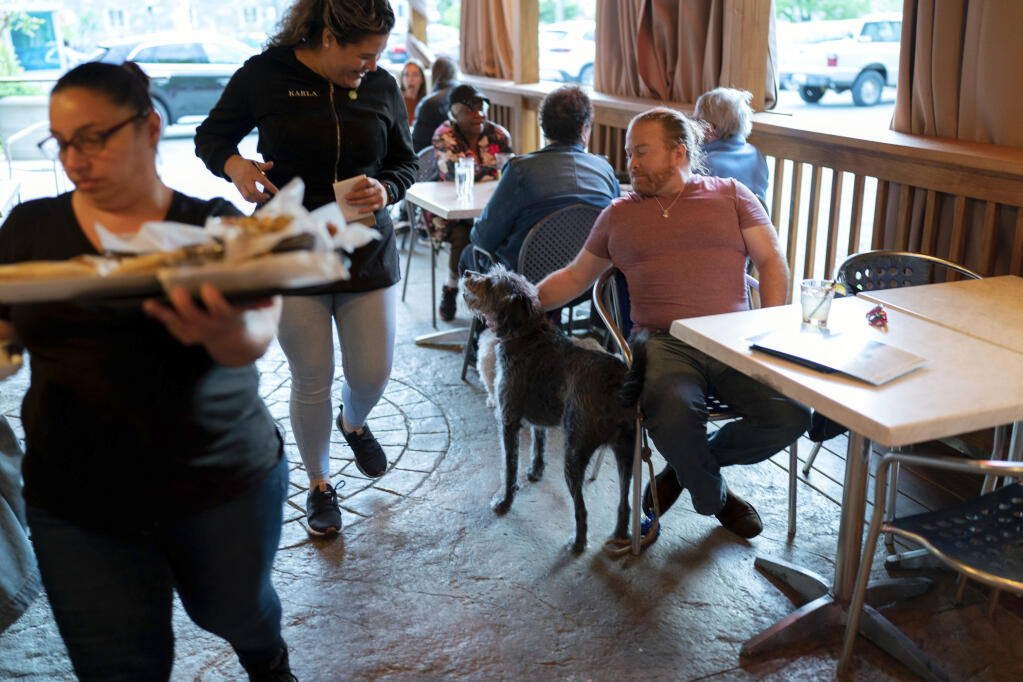 Monty Hobbs and his dog Mattox get ready to order on the patio at the Olive Lounge restaurant in Takoma Park, Md. Thursday, May 4, 2023. Hobbs said Mattox is well-behaved, so it’s nice to know they can drop in at a neighborhood bar if they’re out taking a walk. (AP Photo/Jose Luis Magana)