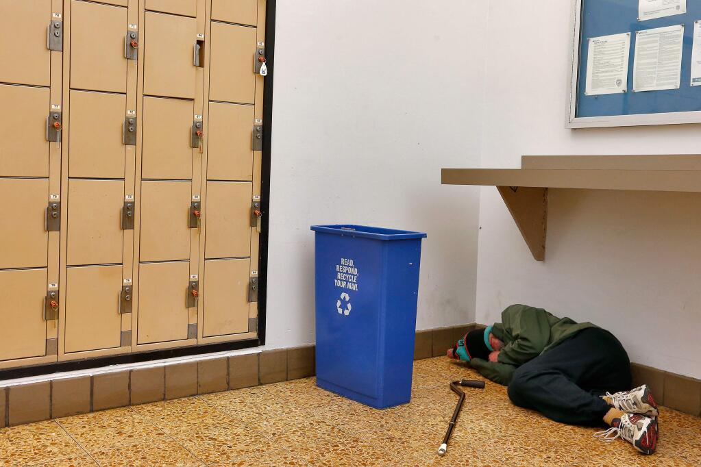 A homeless man sleeps on the floor inside the post office lobby in downtown Santa Rosa, California on Thursday, January 5, 2017. (Alvin Jornada / The Press Democrat)