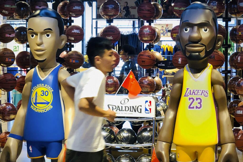 A man walks past statues of NBA players Stephen Curry of the Golden State Warriors, left, and Lebron James of the Los Angeles Lakers holding Chinese flags in the entrance of an NBA merchandise store in Beijing, Tuesday, Oct. 8, 2019. Chinese state broadcaster CCTV announced Tuesday it will no longer air two NBA preseason games set to be played in the country. (AP Photo/Mark Schiefelbein)