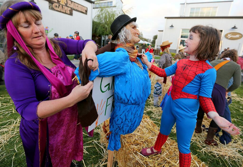 Daniela Kingwill, left, dressed as a queen, and Alina Peterson, 6, right, dressed as spider woman put together a scarecrow during the final night of the Barlow Street Fair in Sebastopol, Thursday, October 30, 2014. (Crista Jeremiason / The Press Democrat)