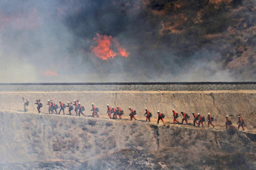 A fire crew approaches as a wildfire burns on Friday, July 22, 2016, in Santa Clarita, Calif. The fire erupted shortly after 2 p.m. Friday next to State Route 14 in Santa Clarita. No homes are immediately threatened, but fire officials say evacuations have been ordered from Soledad Canyon to Agua Dulce Canyon Road. (Katharine Lotze/The Santa Clarita Valley Signal via AP)