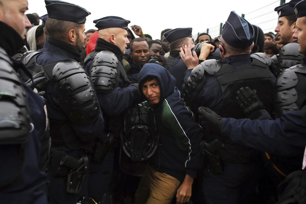 A migrant makes his way through a police cordon in the makeshift migrant camp known as 'the jungle' near Calais, northern France, Monday Oct. 24, 2016. French authorities are beginning a complex operation, unprecedented in Europe, to shut down the makeshift camp, uprooting thousands who made treacherous journeys to escape wars, dictators or grinding poverty and dreamed of making a life in Britain. (AP Photo/Thibault Camus)