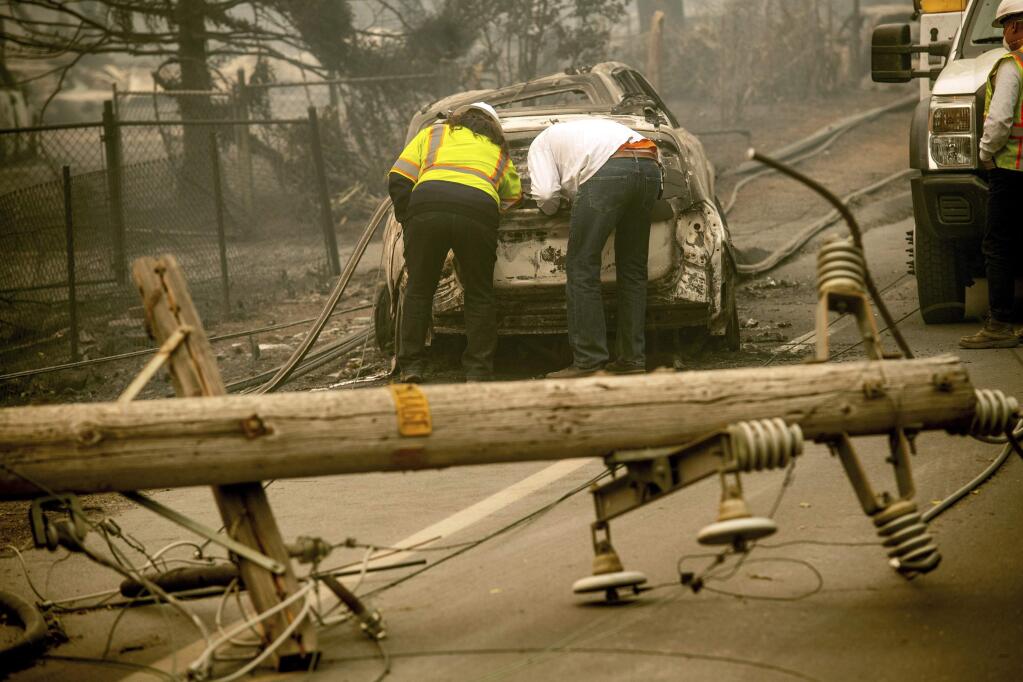 FILE - In this Nov. 10, 2018, file photo, with a downed power utility pole in the foreground, Eric England, right, searches through a friend's vehicle after the wildfire burned through Paradise, Calif. Pacific Gas & Electric's key lenders have offered a $30 billion plan to pull the utility out of bankruptcy, and give the tarnished company a new name. The Sacramento Bee reports the proposal filed Tuesday, June 25, 2019 in U.S. Bankruptcy Court would set aside up to $18 billion to pay claims on the 2017 and 2018 wildfires caused by PG&E equipment. (AP Photo/Noah Berger, File)