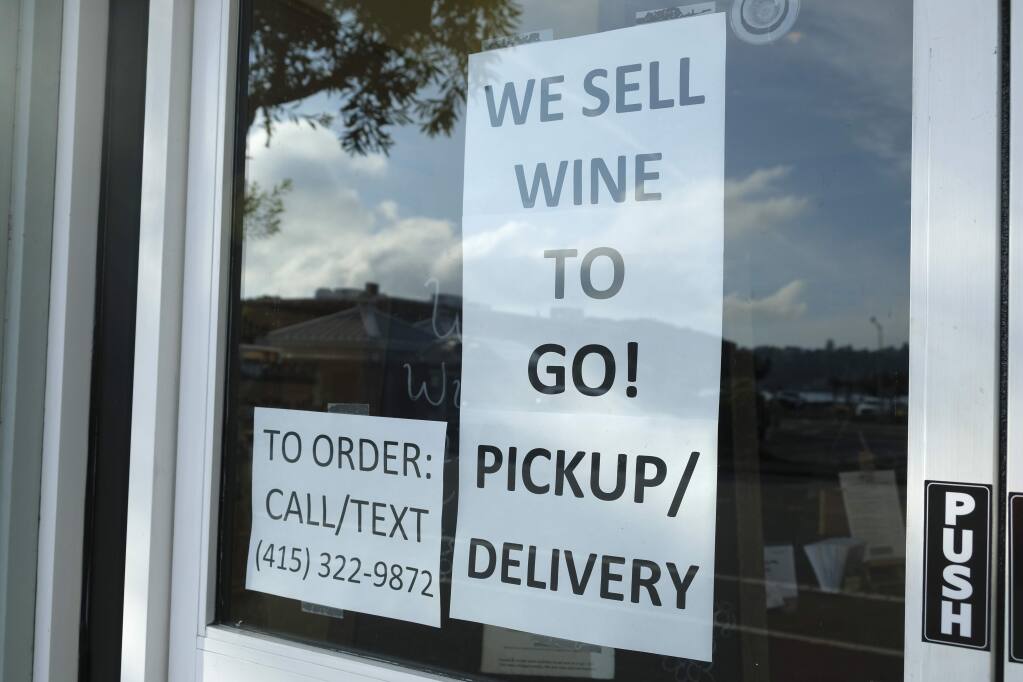 A sign in the window of The Bacchus & Venus advertises they are selling wine to go  March 17, 2020, in Sausalito. The allowance of restaurants to sell beverage alcohol to go was among dozens of accommodations the California Bureau of Alcoholic Beverage Control made for businesses significantly impacted by coronavirus pandemic public health limitations on commercial activity. A lingering legal question is how many of these allowances will become permanent. (AP Photo/Eric Risberg)
