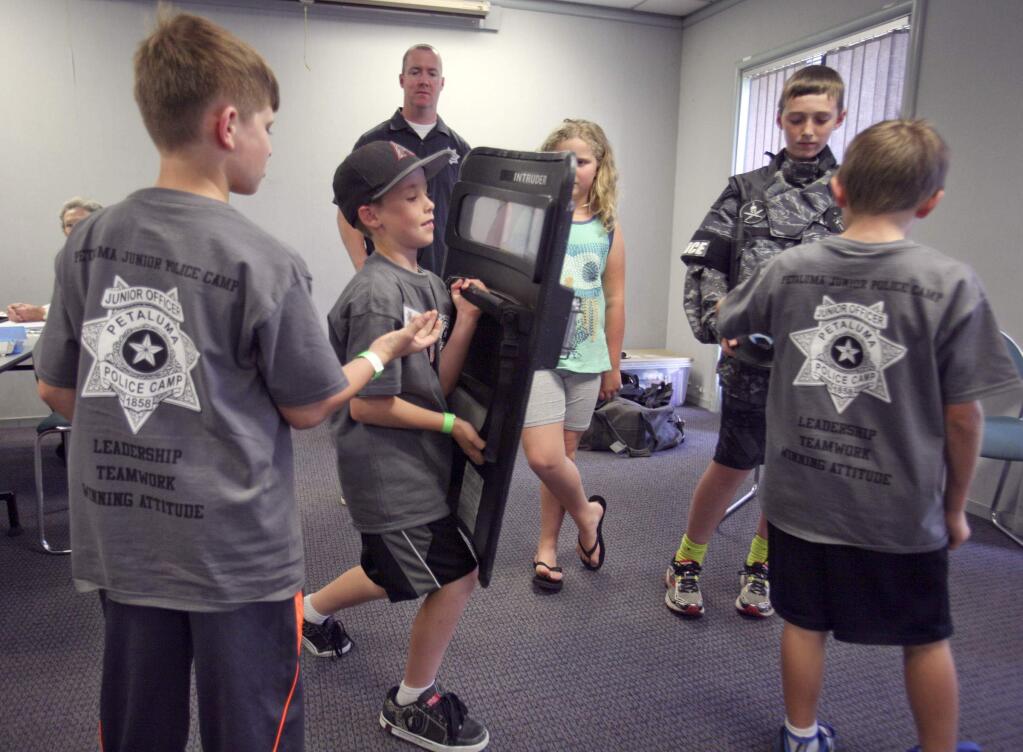 Dylan Gard, 9, checks out SWAT shield with Joseph Lauritzen, 10, left, and Harrison Williams, 10, after a SWAT demonstration by Sgt. Paul Gilman, background, while Gilman's kids Colin, in SWAT uniform, and Corrine look on during the Petaluma Police Department Junior Police Officer Camp at Lucchesi Center in Petaluma on Monday, March 23, 2015. (SCOTT MANCHESTER/ARGUS-COURIER STAFF)