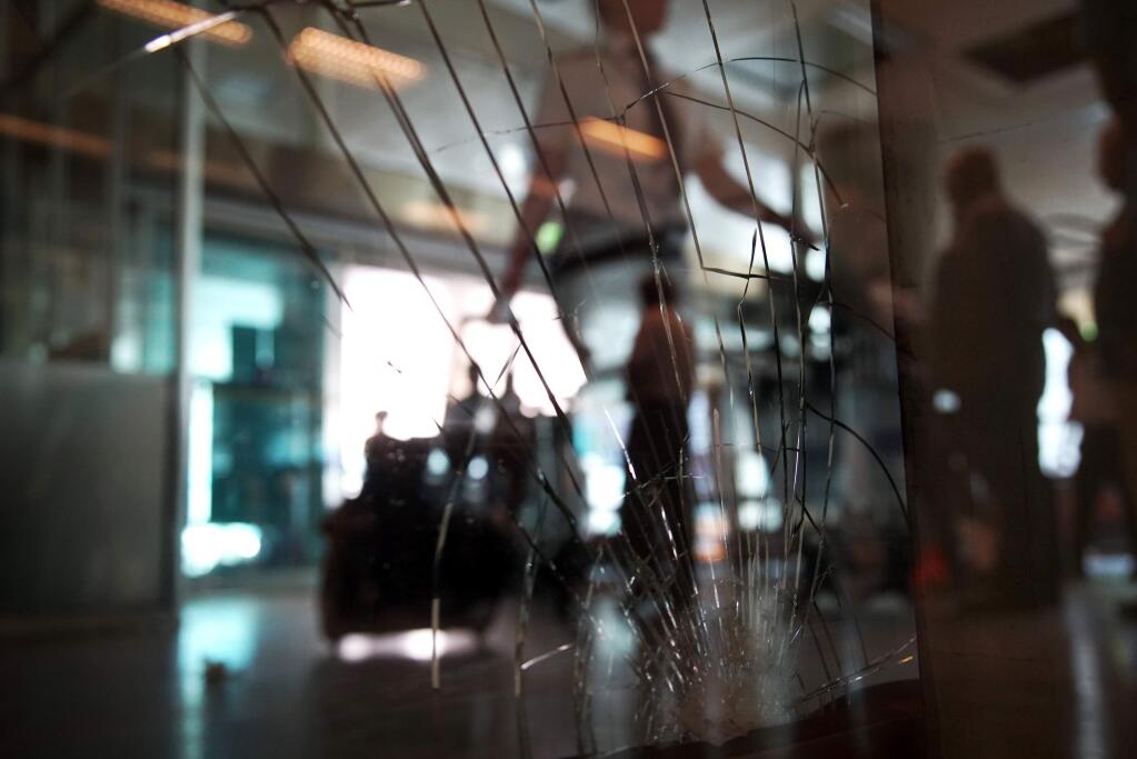 A traveler passes a broken windows at the arrivals hall at Ataturk Airport, Wednesday, June 29, 2016. Suicide attackers killed dozens and wounded more than 140 at Istanbul's busy Ataturk Airport late Tuesday, the latest in a series of bombings to strike Turkey in recent months. Turkish authorities have banned distribution of images relating to the Ataturk airport attack within Turkey.(AP Photo/Bram Janssen)