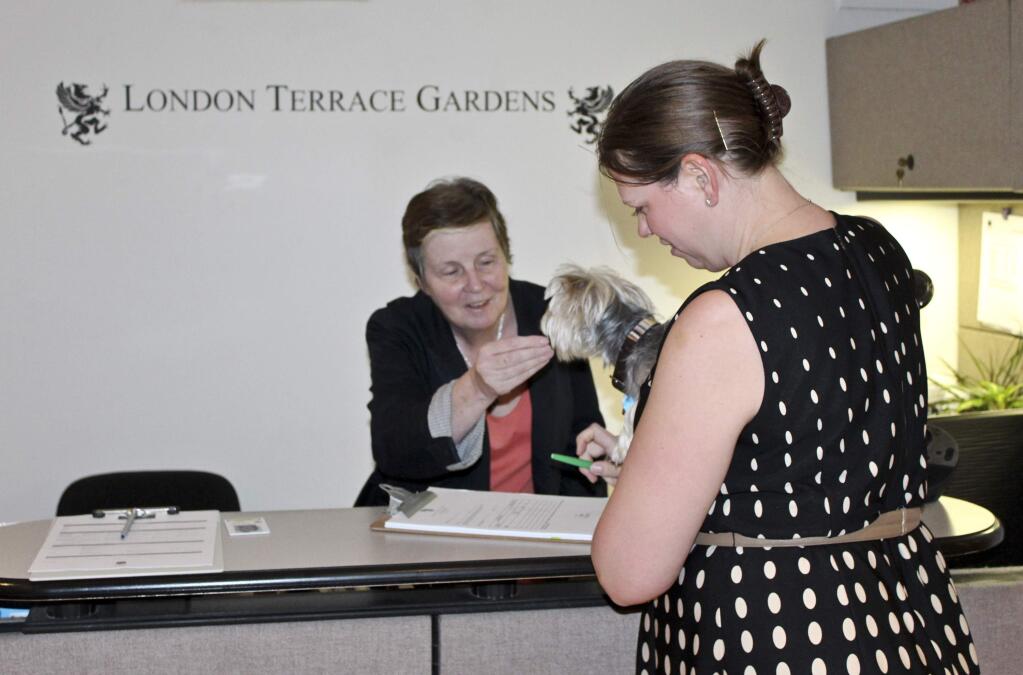 In this Wednesday, Oct. 15, 2014 photo, Ellen Bornet, of Rose Associates, left, general manager of London Terrace Gardens in New York, greets resident Lisa Bulloch-Jones and her Maltese-Yorki mix, Marley, as Bulloch-Jones fills out a permission to enter form for her dog walker. Pet security deposits register in the hundreds of dollars and are getting steeper. (AP Photo/Rose Associates, Rebecca Koppel)