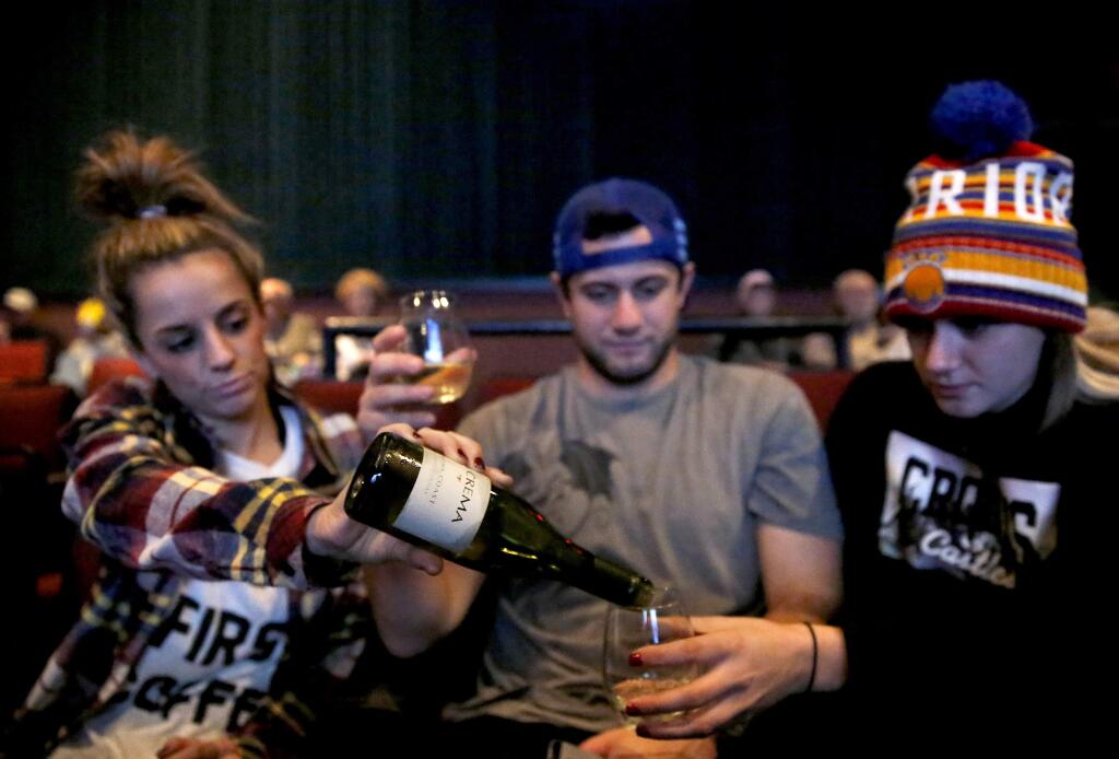 (From left) Siblings Lisa McCabe, Richard Tigner, and Becky Tigner pour a bottle of wine in the theater at the Raven Film Center in Healdsburg, California on Sunday, December 21, 2014. (BETH SCHLANKER/ The Press Democrat)