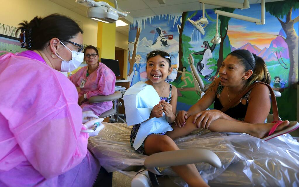 Lucero Gutierrez, 7, smiles after dentist Ramona English, left, uses a finger to show how a polisher feels while her mother Mayra Hermosillo of Petaluma tries to alleviate her fears at the new Rohnert Park Health Center on Thursday. (JOHN BURGESS / The Press Democrat)