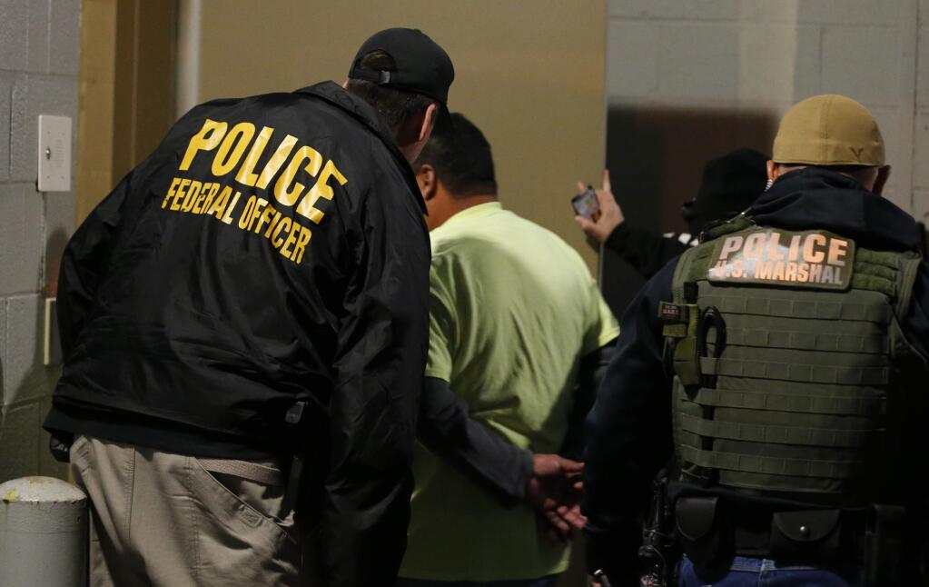 FILE - In this Oct. 22, 2018, file photo U.S. Immigration and Customs Enforcement agents escort a target to lockup during a raid in Richmond, Va. Carrying out President Donald Trump's hard-line immigration policies has exposed ICE to unprecedented public scrutiny and criticism, even though officers say they're doing largely the same job they did before the election, prioritizing criminals. (AP Photo/Steve Helber, File)
